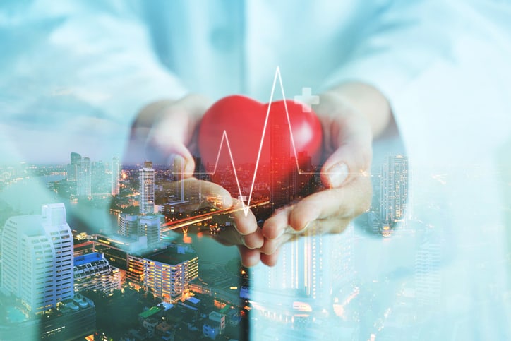 Double exposure of medical doctor holding red heart shape with city night background